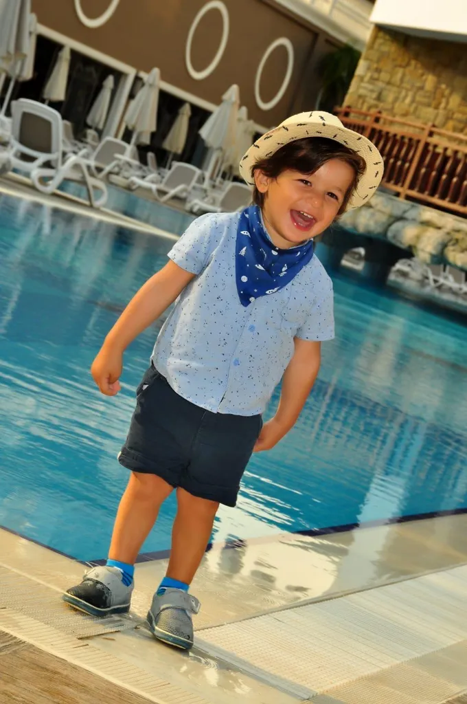 Havuz kenarında hasır şapkalı, gülen bir çocuğun fotoğrafı